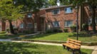 open green grass area with a bench outside apartment entrances 