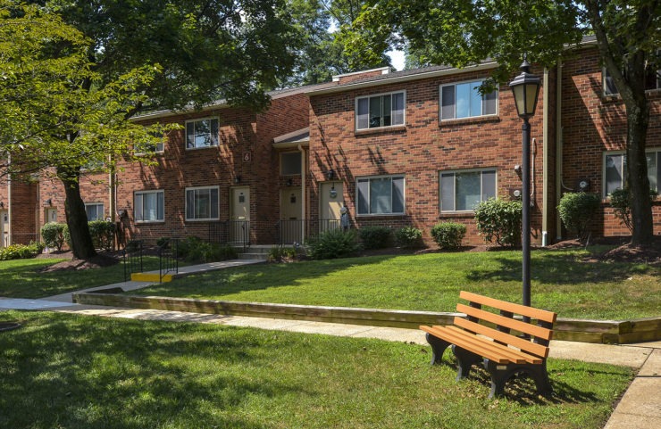 open green grass area with a bench outside apartment entrances 