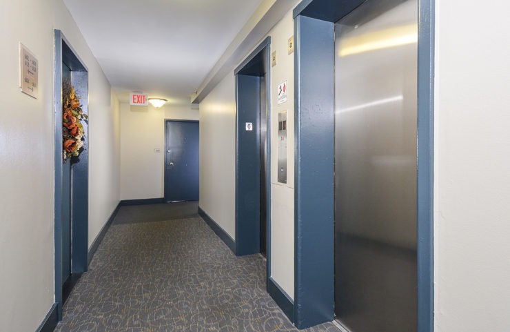 elevators and hallway with blue doors to enter apartment homes