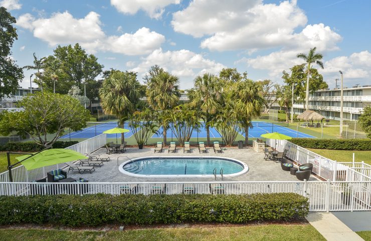 aerial view of pool with surrounding white fence and palm trees