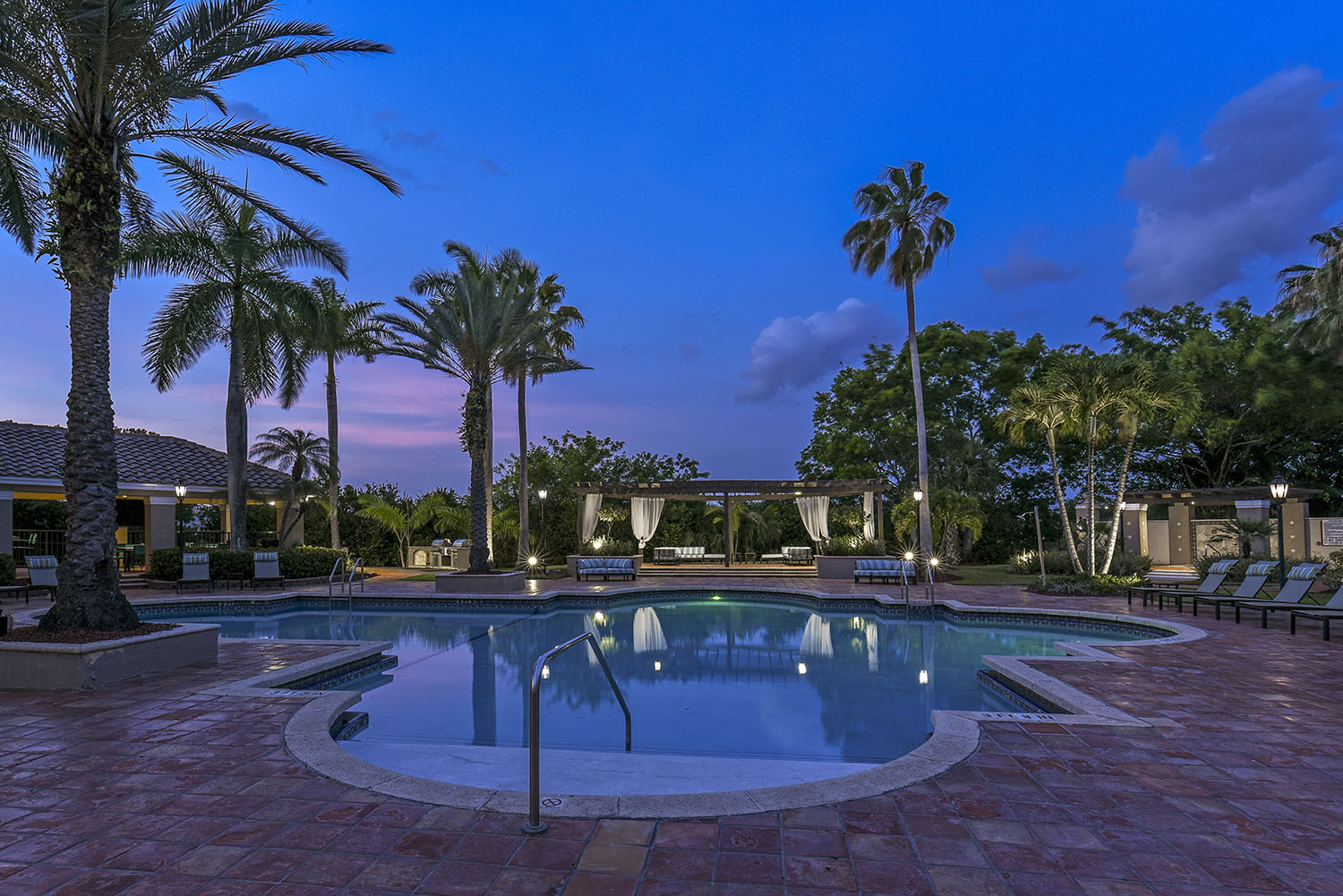 Pool at dusk with palm trees and cabana views.
