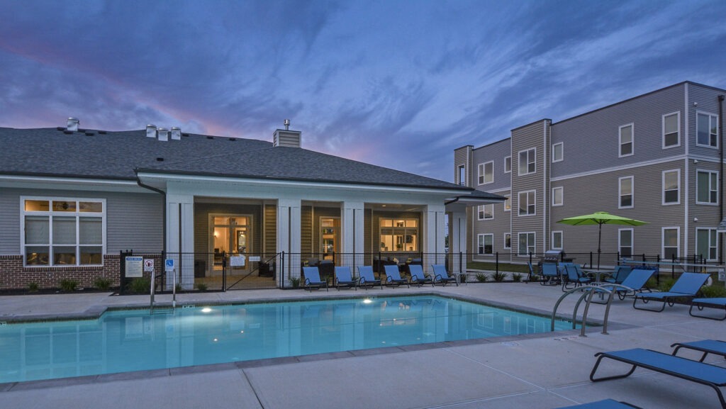 Westside clubhouse with a pool and several chairs during dusk