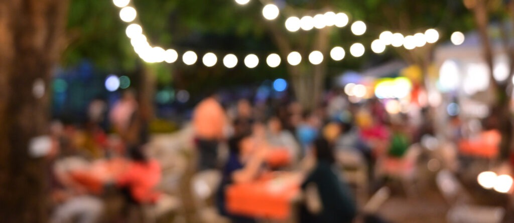 people crowd in night party festival of outdoor garden with light bulb hanging decoration, image blur used for celebration background