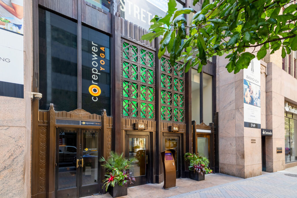 Street view of 1616 walnut with a large sign reading "CorePower Yoga" indicating the fitness center inside. The front of the building has art deco designs and potted plants