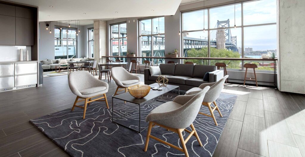 Co-working lounge with several chairs, couches, tables, and kitchenette with a sprawling view of the Ben Franklin Bridge out the floor-to-ceiling windows.