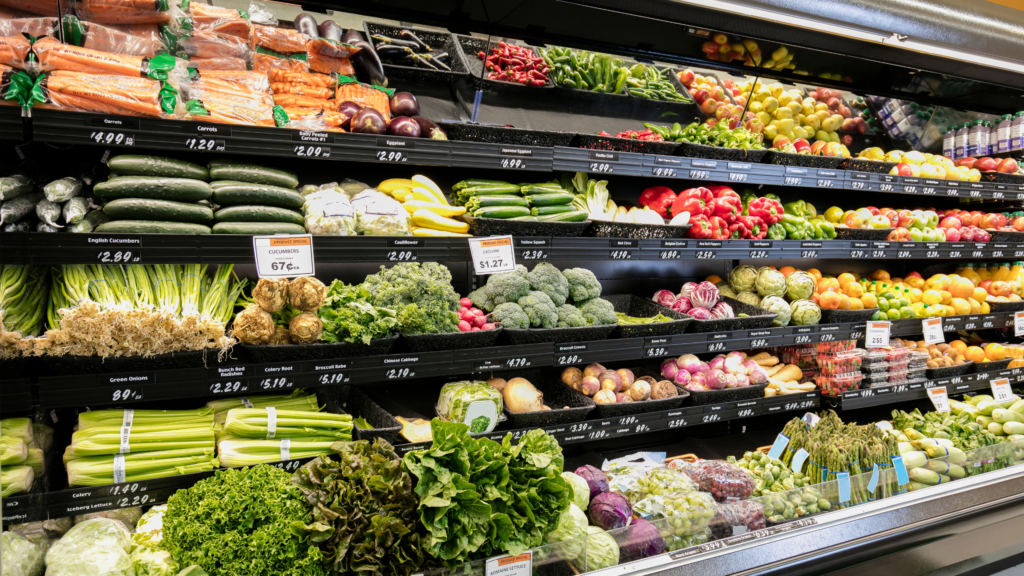 A grocery store produce section with a bunch of fresh vegetables like onions, peppers, and lettuce