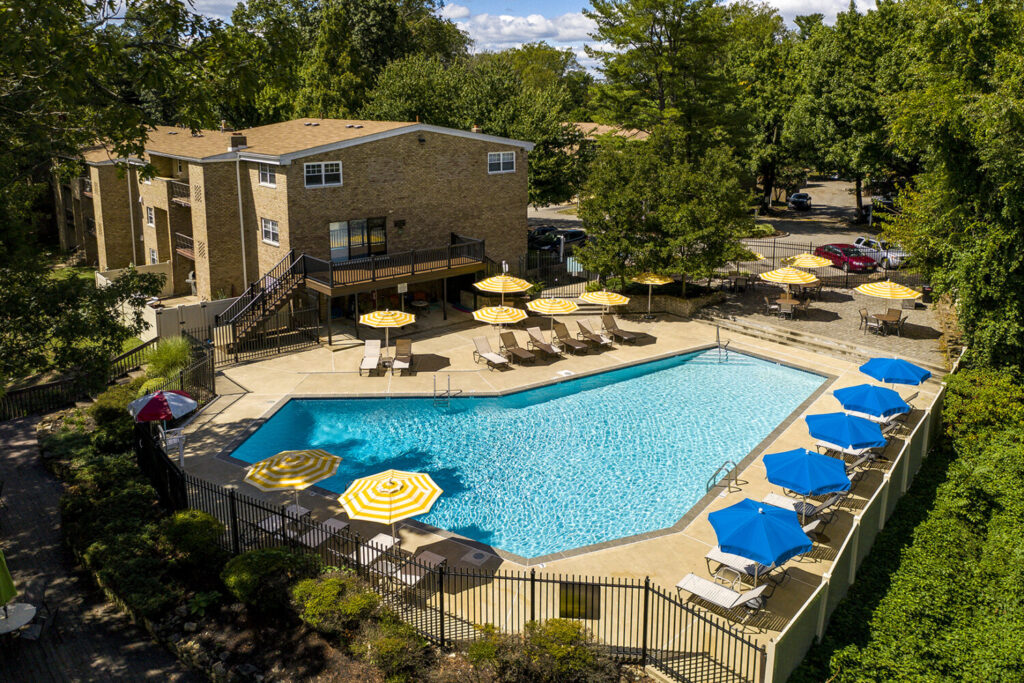 Radnor Crossing leasing office and apartments next to their outdoor pool. The pool has several umbrellas, lounge chairs, and a lifeguard stand.