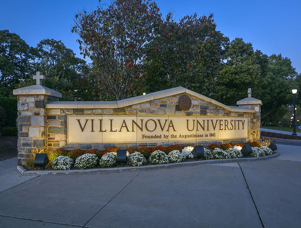 A stone sign reading "Villanova University" with red and white flowers planted in front of it