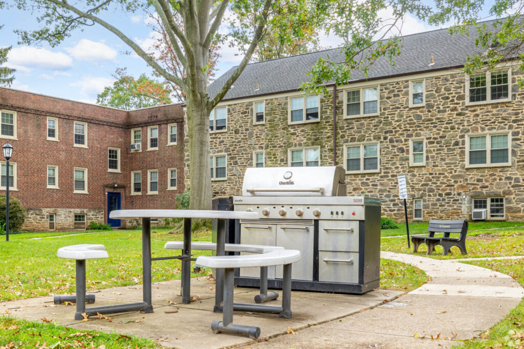 A courtyard area surrounded by brick and stone buildings. A grill with a picnic table next to it.