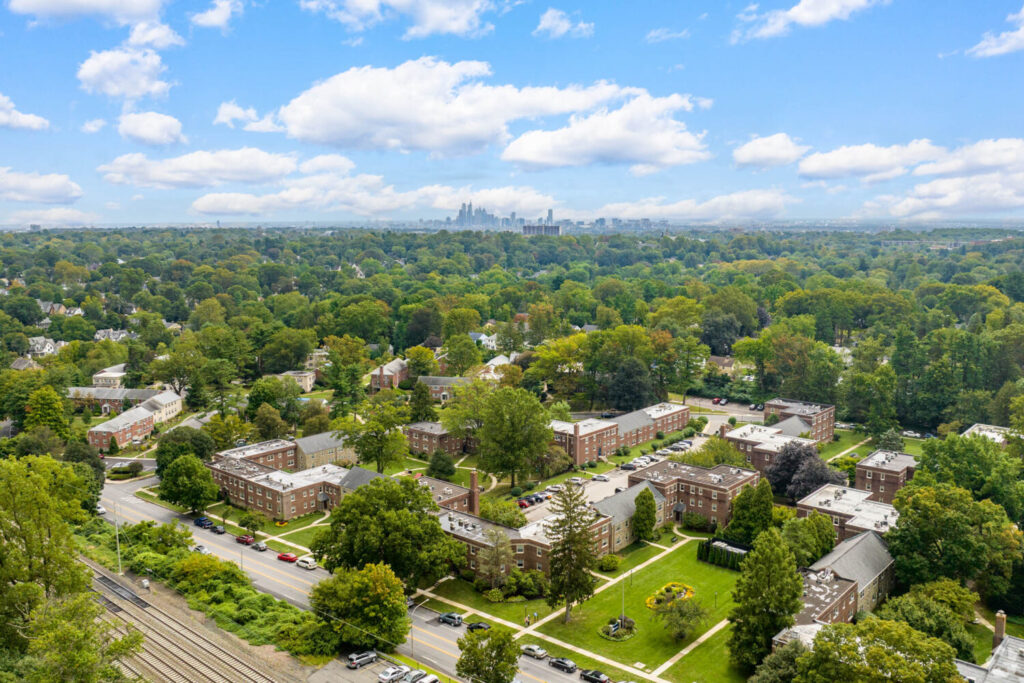 A drone view of the 14-acres of land that the Wynnewood is on. Covered in green trees and beautiful grass. The Philadelphia skyline is behind.