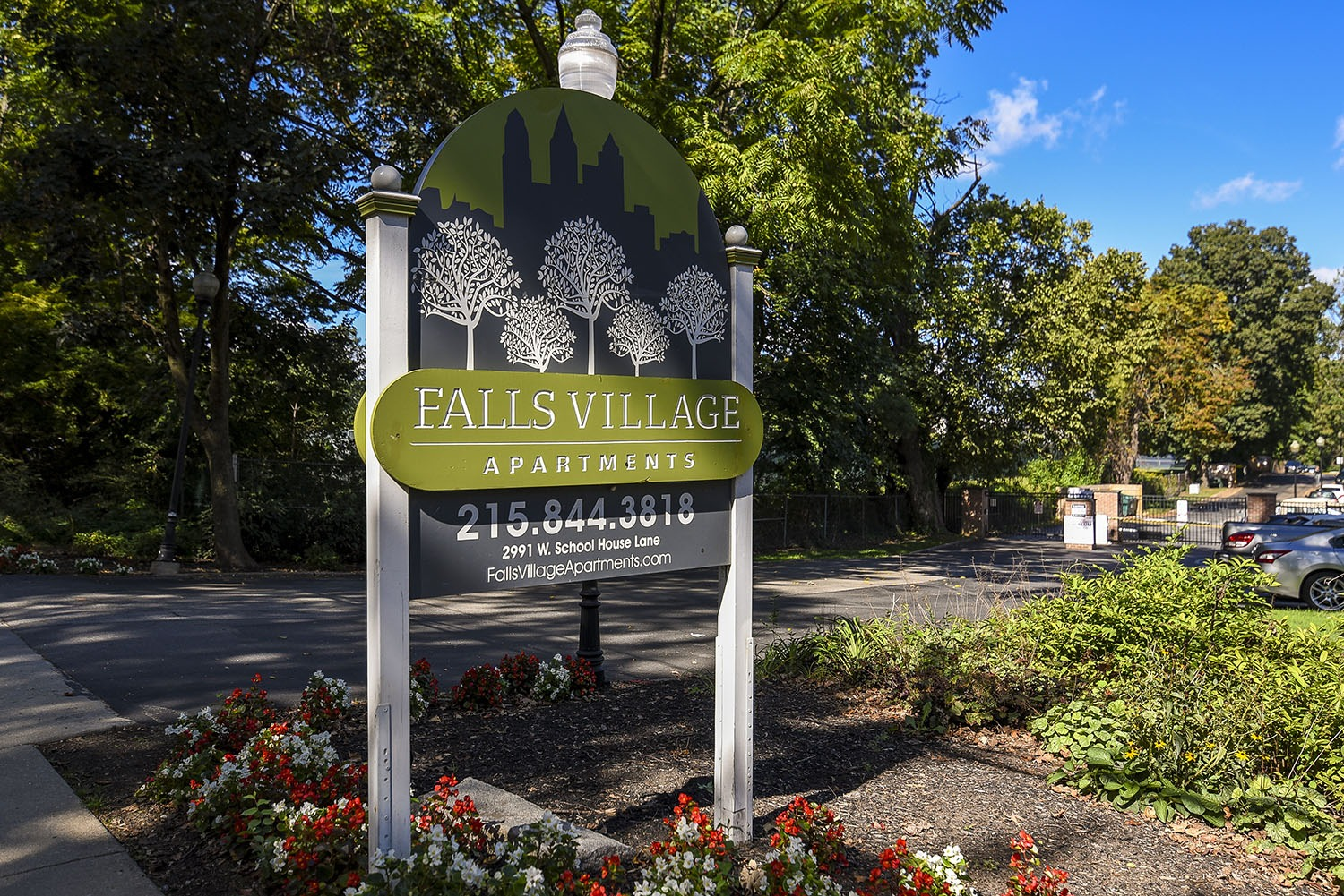 A blue and green sign with white trees and words that read "Falls Village Apartments"