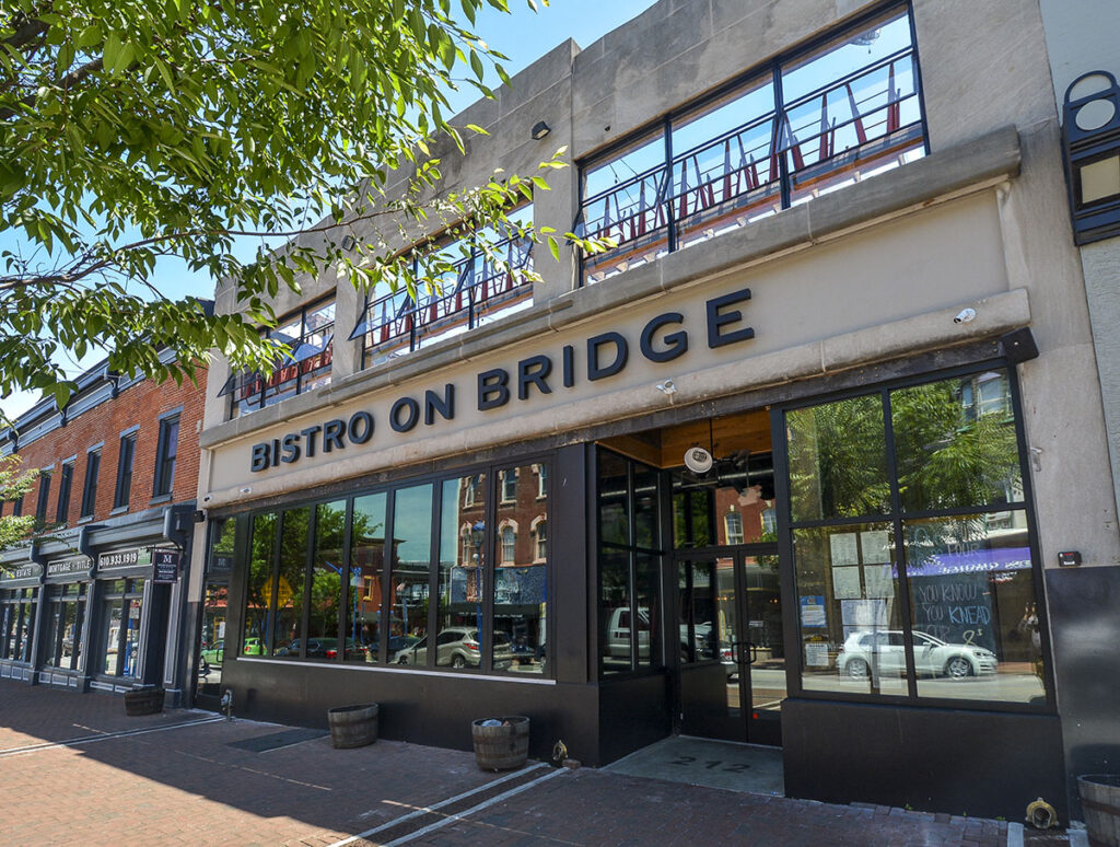 Old tan stone building with black window frames with the words "Bistro on Bridge" written across the top