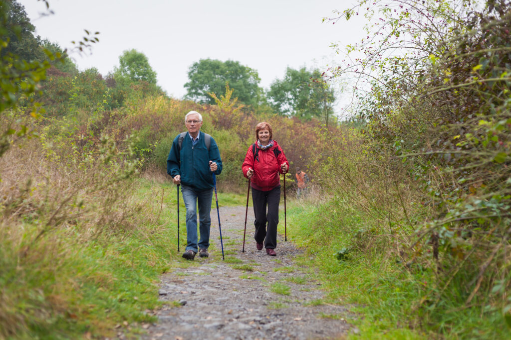 A couple hiking with Nordic walking poles surrounded by greenery ona  dirt path