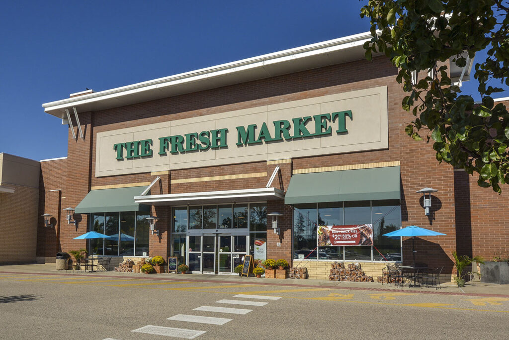 A grocery store in a brick building with the green letters reading "The Fresh Market"
