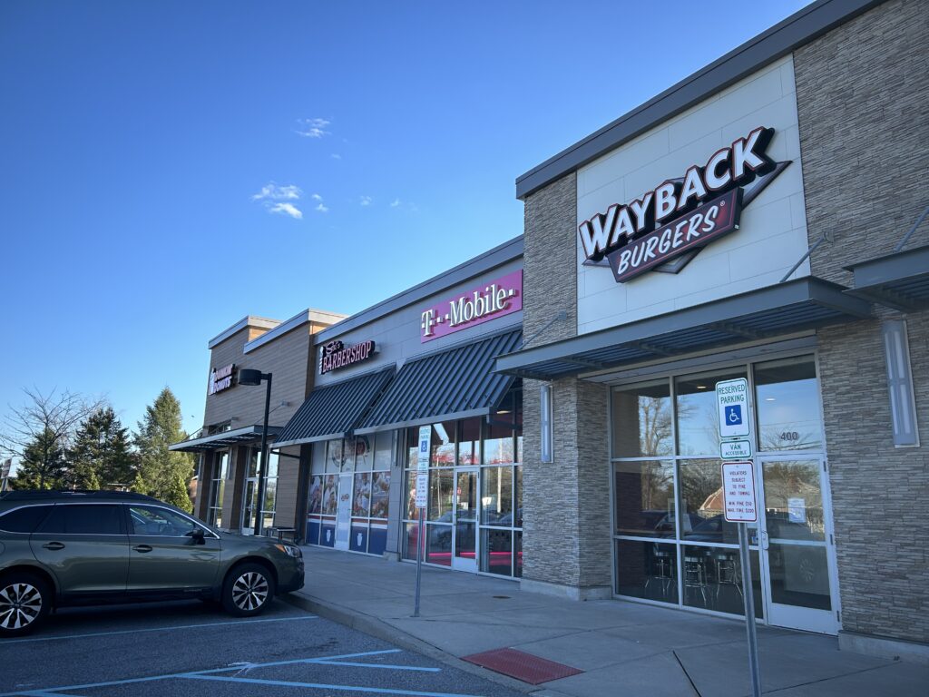 Side of a building showing the signs for Wayback Burgers, T-Mobile, Sal's Barbershop, and Dunkin Donuts