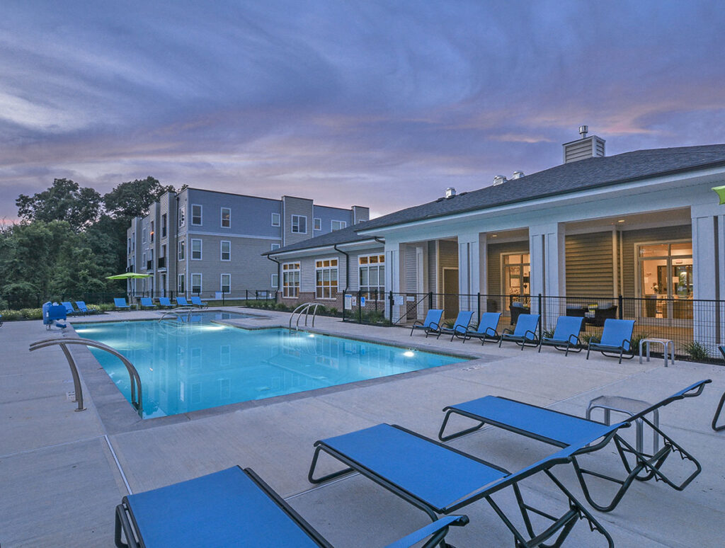A pool during a summer afternoon outside of the Clubhouse building. Blue lounge chairs sit on the side of the pool and the sky is a blueish pink