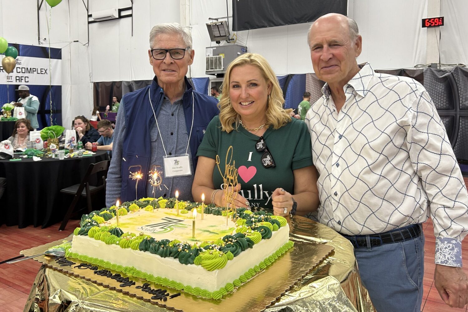 Jim, Jessica, and Michael Scully smiling and standing in front of a green birthday cake with candles in it