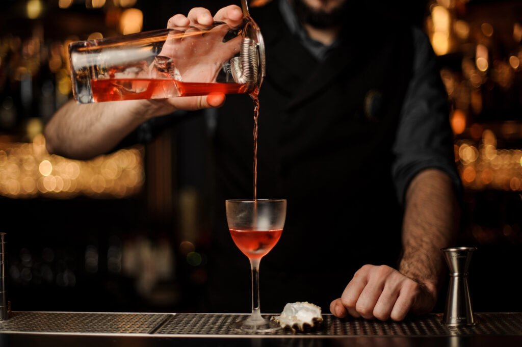 Bartender pouring a craft cocktail in front of string lights