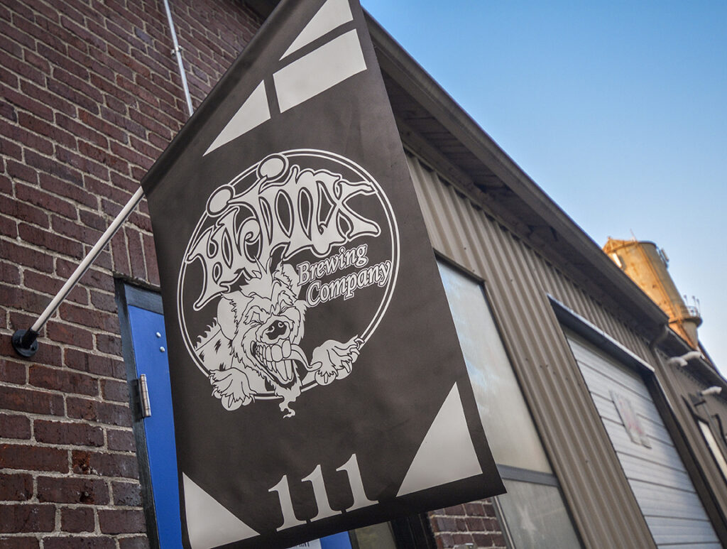 Brown sign in front of a warehouse brewery that reads "HiJinx Brewing Company"
