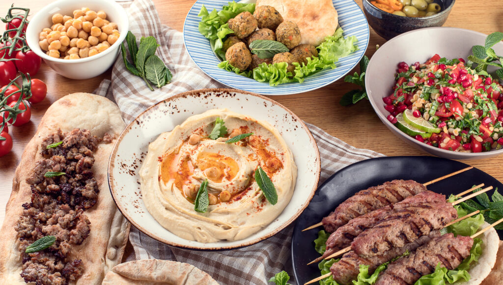 A table full of Middle Eastern food including hummus, falafel, pita, and kebabs.