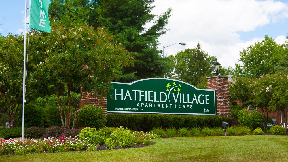 Green sign reading "Hatfield Village Apartments" surrounded by trees