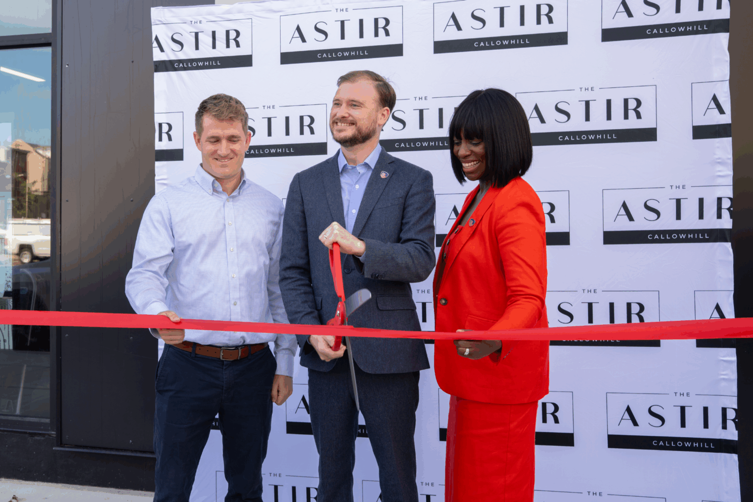 Three people with large scissors cutting a red ribbon