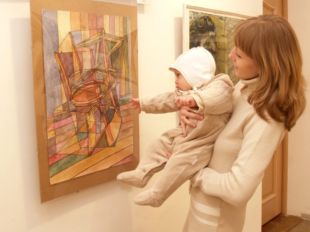 Woman holding a small child in front of a painting in a museum