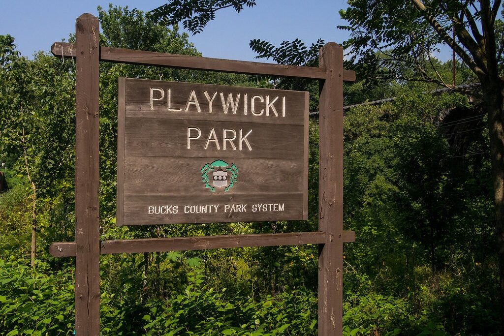 Wooden sign in front of trees and bushes reading "Playwicki Park"