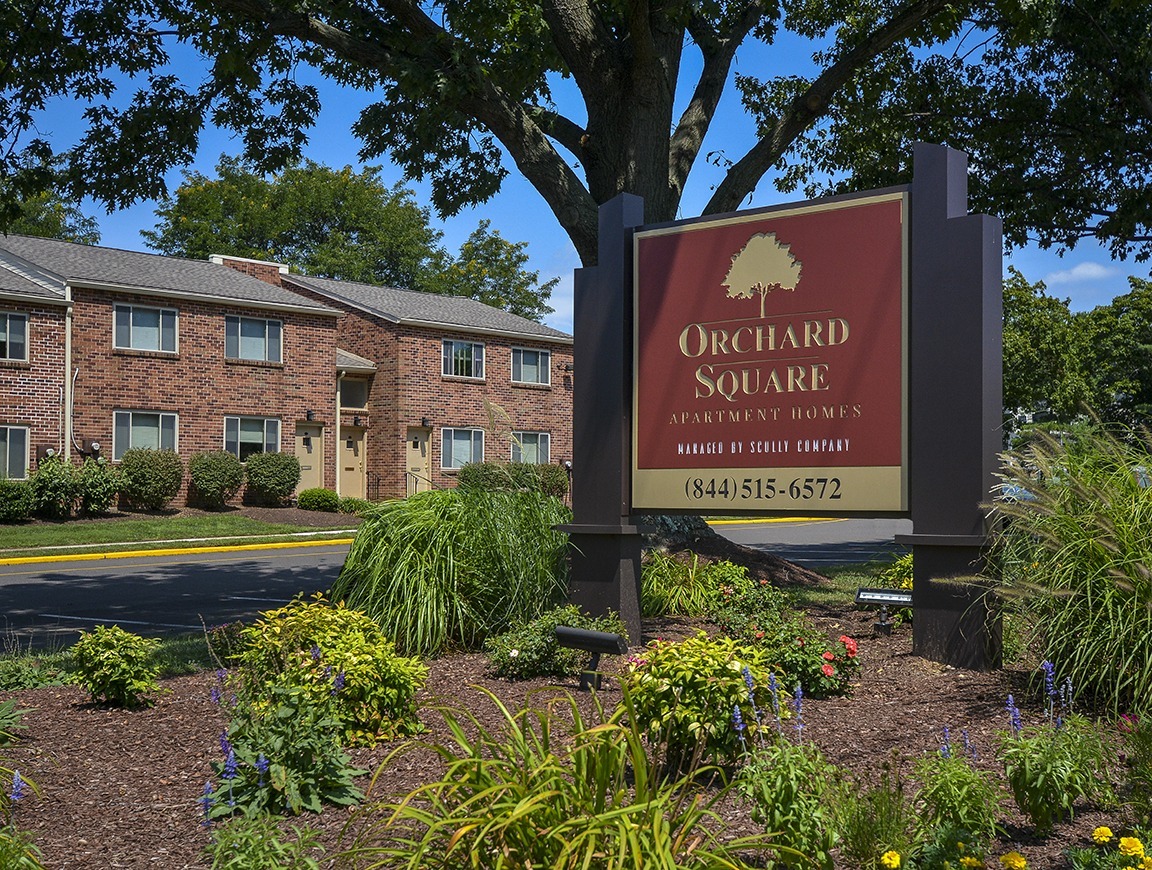 Orchard Square apartments with a sign in front surrounded by trees