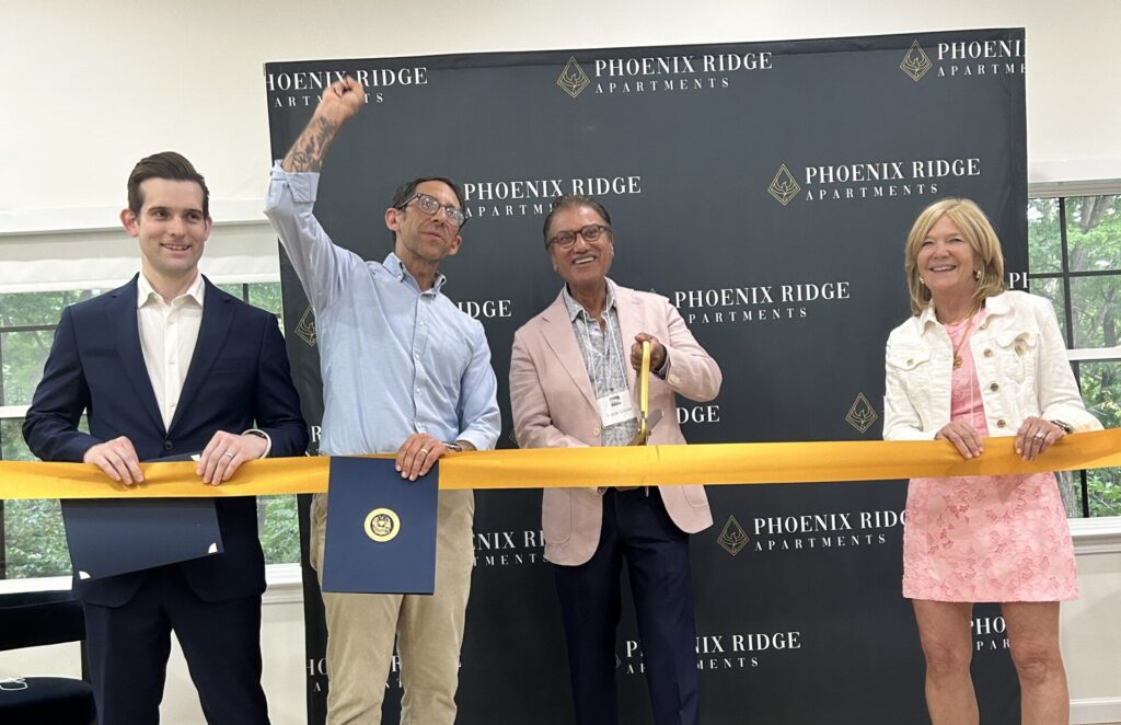 Four people with a gold ribbon doing a ribbon cutting ceremony